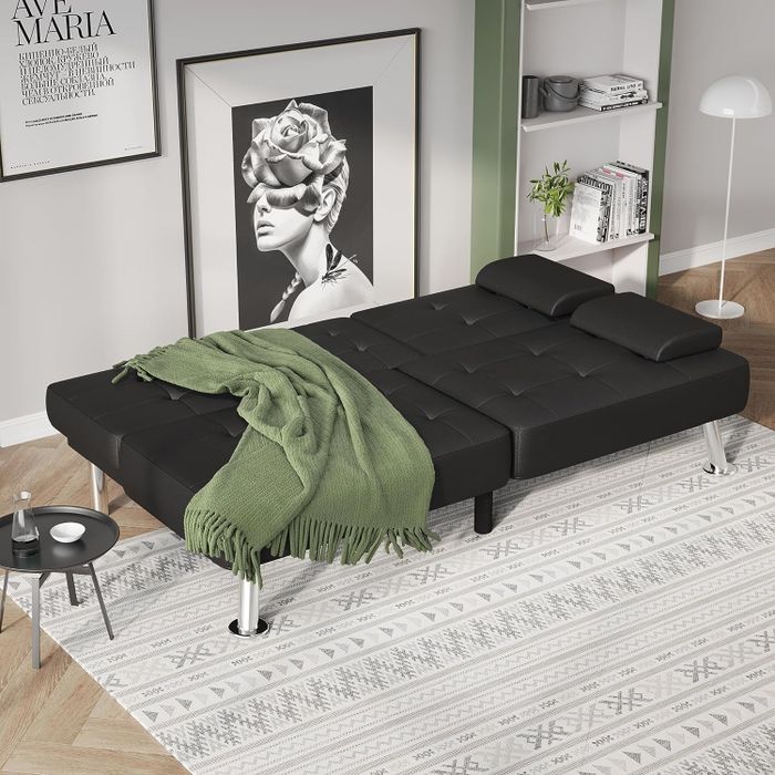the black faux leather futon sofa in its flat position with a blanket draped over it