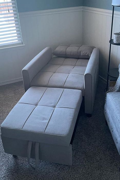 A convertible sofa bed in a living room, shown in its extended bed position with a pillow on top.