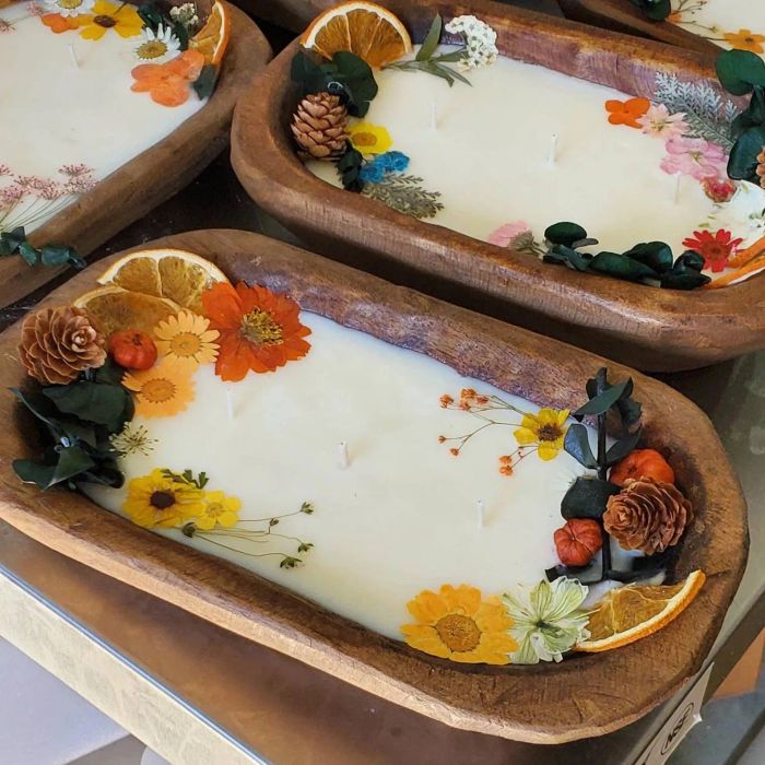 Two wooden dough bowls filled with white candle wax, surrounded by natural flowers and pinecones, arranged on a tray for a rustic touch.