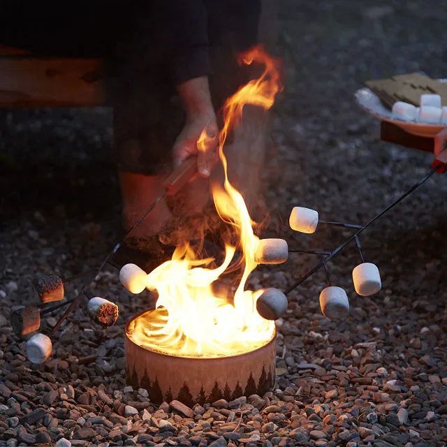 A group of people roasting marshmallows by the portable campfire.