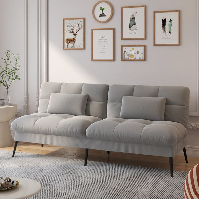A modern gray sofa with pillows, set in a stylish living room, featuring framed artwork on the wall and a small plant on the side table.