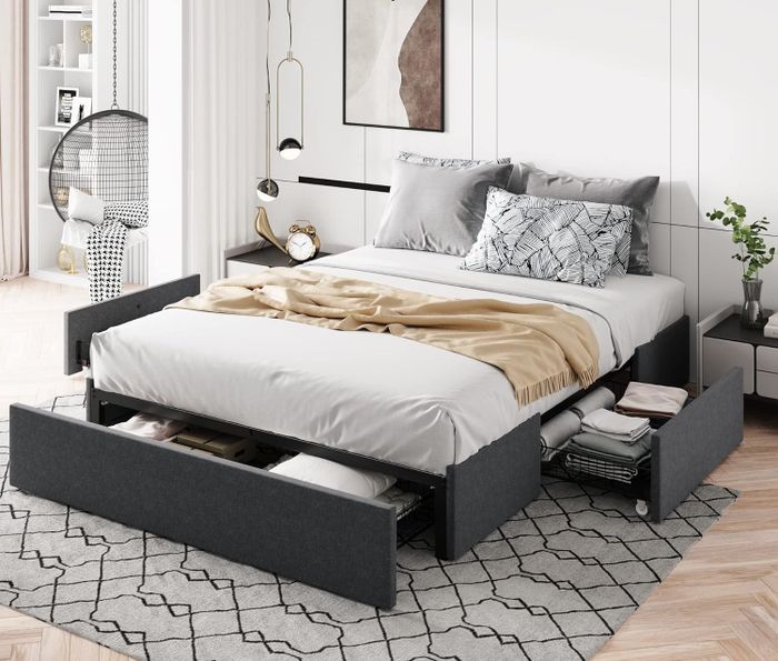 A cozy, modern bedroom featuring a minimalist bed with storage drawers beneath. The bed is adorned with pillows, a beige blanket, and tasteful wall decor.