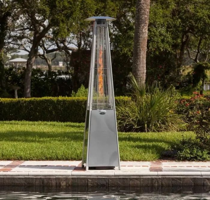 A stainless-steel patio heater illuminated beside a pool outdoors, creating warmth and ambiance.