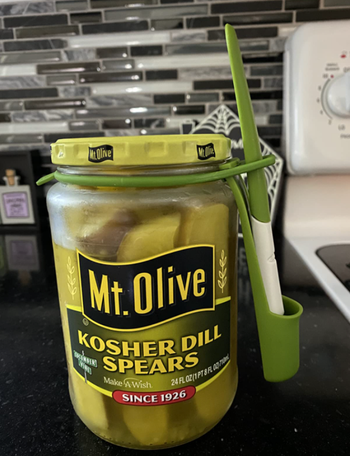 The pickle fork neatly held in a silicone utensil holder wrapped around the lid of a pickle jar