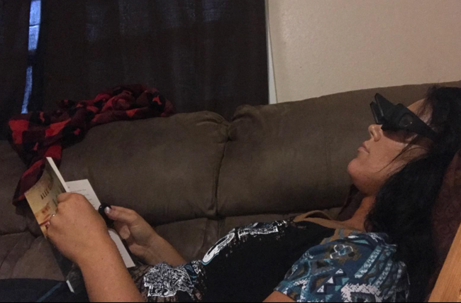 A reviewer lounging on the couch, using the glasses while reading a book in an upright position