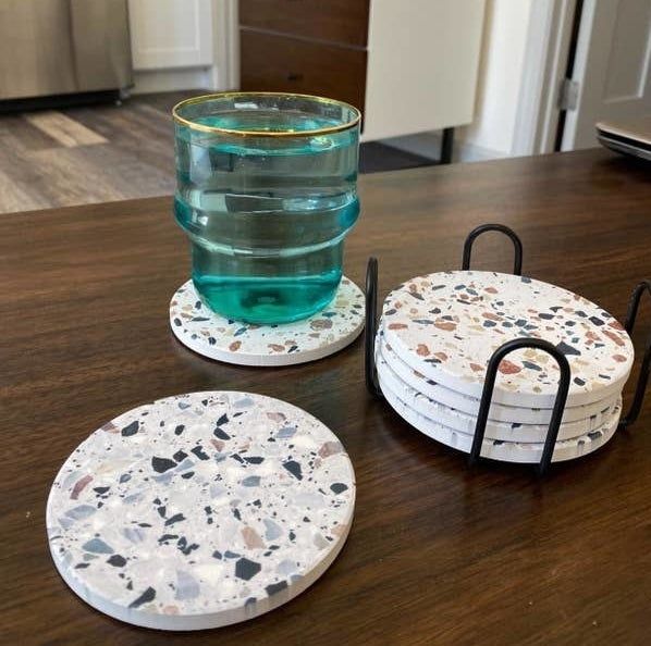 A set of four coasters neatly stacked in their stand, with one coaster shown individually and another holding a blue cup.