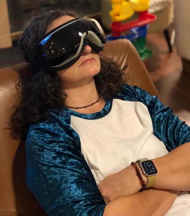 A reviewer wearing a sleek, black goggle-like eye massager