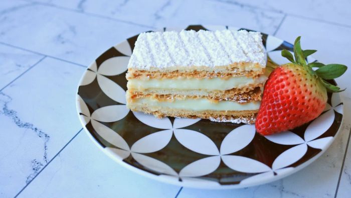 A perfect slice of mille-feuille served on a plate, accompanied by a fresh strawberry.