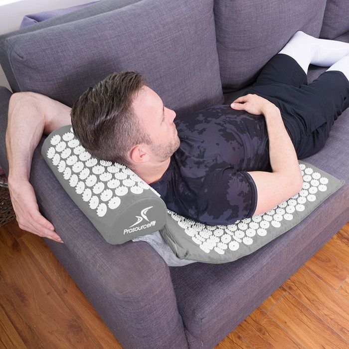 A model lounging on a gray mat covered with circular acupressure spikes on a couch