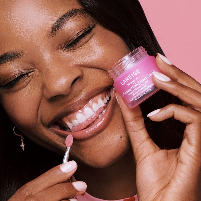 Model holding a pink carton of the lip mask and using a small applicator