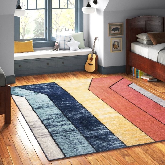 A modern rug with a geometric pattern adds style to a cozy bedroom featuring wooden floors, a bed, and a window seat, creating a beautifully designed space.