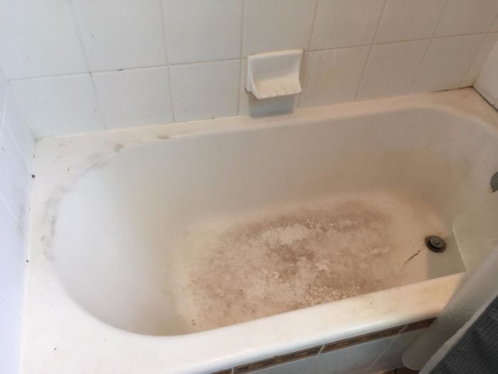 A white bathtub with dark brown stains in the corners and on the floor