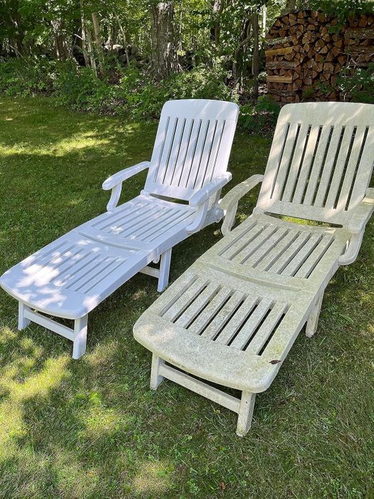 Two outdoor lounge chairs sitting on a grassy lawn, one looking fresh and clean, while the other appears weathered and worn, with trees and a woodpile in the background.