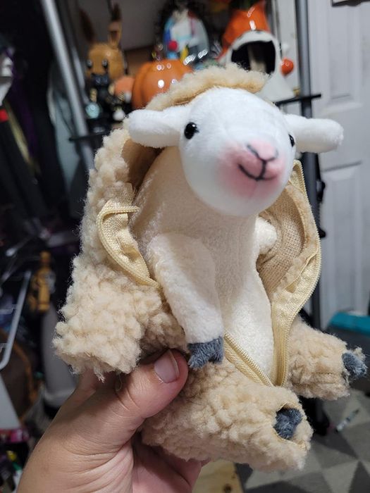 A hand holding a plush sheep designed as a backpack, offering a cozy and distinctive way to store items