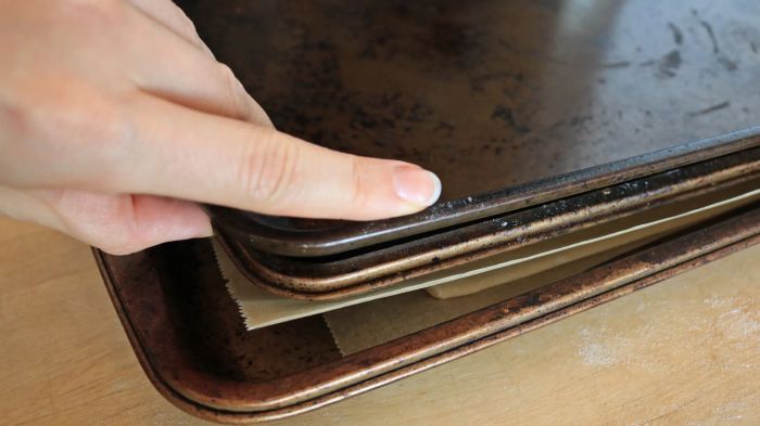A hand carefully stacking sheet pans on top of one another.