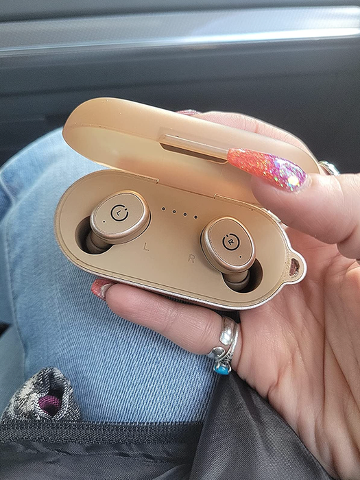 A reviewer holding the light pink version of the headphones