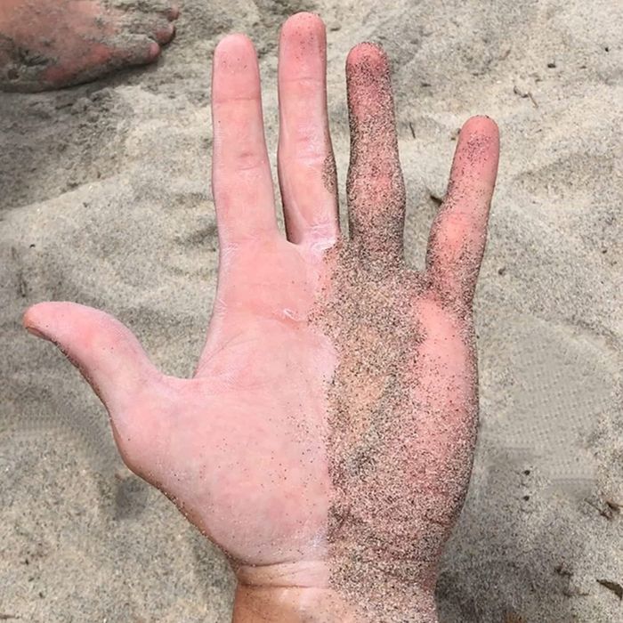 A hand, half covered in sand and half clean, free of sand