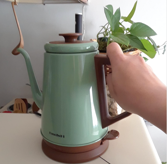 Reviewer holding the lid of a pale seafoam green kettle with brown accents.