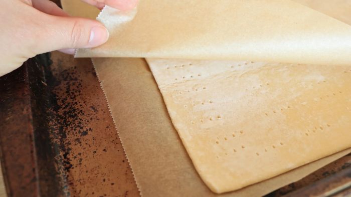 A hand carefully removing parchment paper from a sheet of puff pastry.