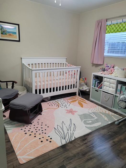 A cozy nursery featuring a white crib, a patterned rug, a rocking chair, a small bookshelf, and decorative touches such as plush toys and a painting on the wall.
