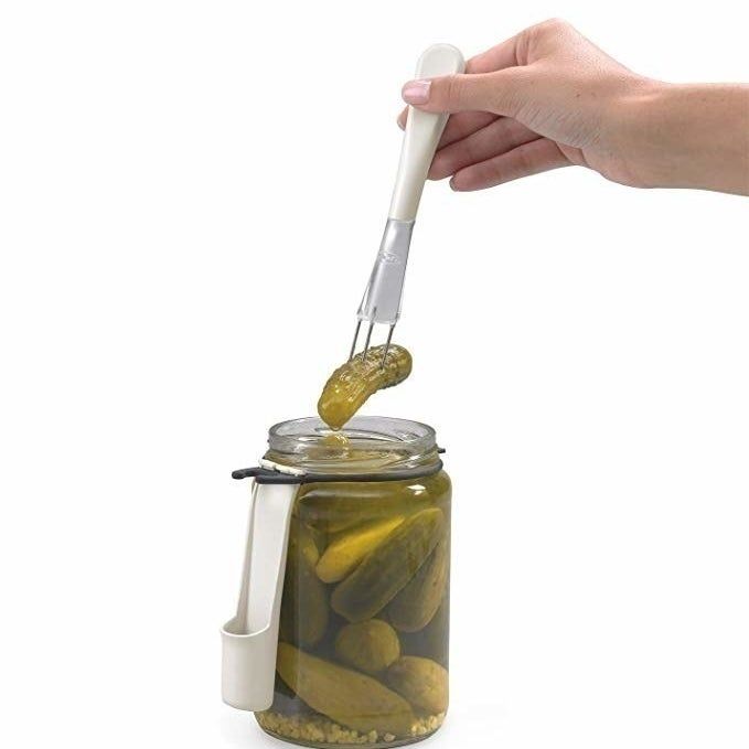 A person using a fork to retrieve a pickle from a jar