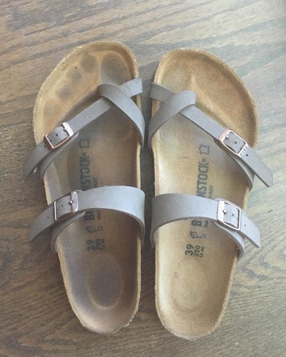 A reviewer displays a pair of sandals with suede soles, one showing a dirty foot outline and the other clean after using the brush