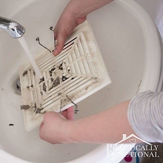A blogger's hands washing the exhaust fan cover in the sink.