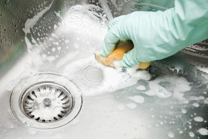 hand scrubbing the sink with soap and a sponge
