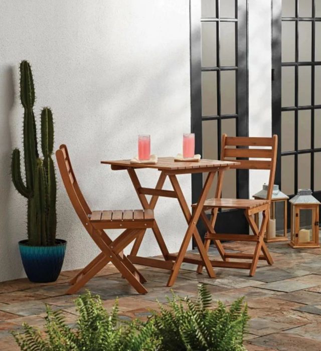 A medium wood bistro table and matching chairs, nestled in a beautifully decorated patio setting.