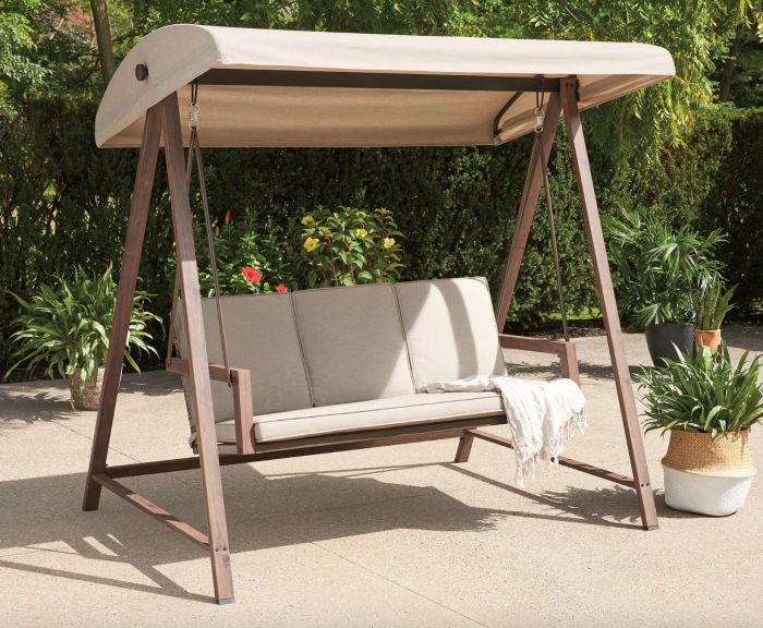 A tan porch swing complete with a matching canopy, placed in a beautifully decorated outdoor space.