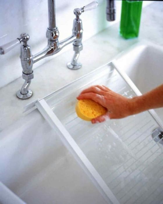 A hand washing a glass shelf from the fridge in the sink.