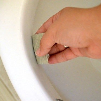 A hand placing duct tape under the rim of a toilet.