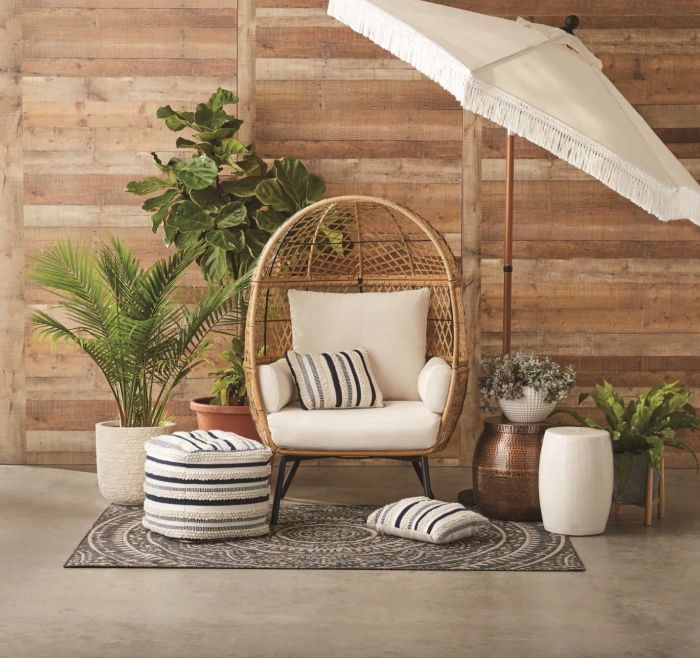 A tan rattan egg chair with soft white cushions, placed in a tastefully designed patio area.