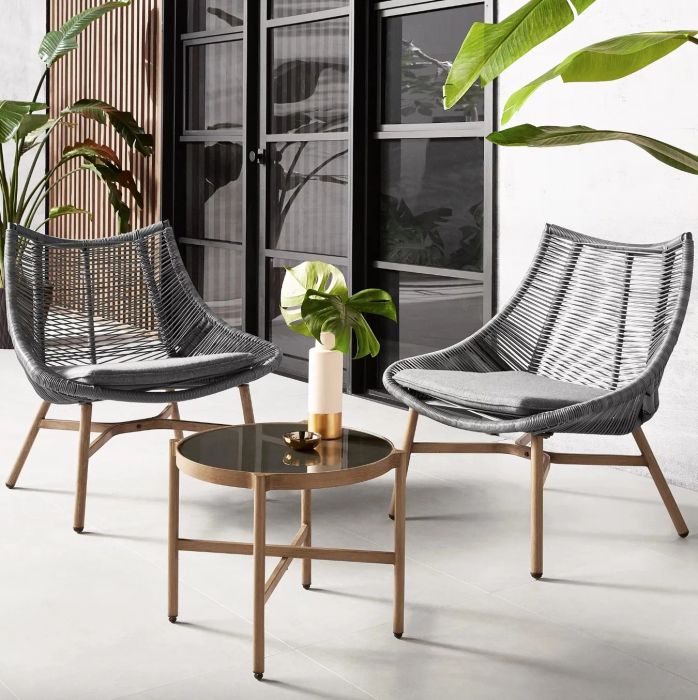 Grey chairs with wooden legs paired with a glass-topped side table, set in a beautifully decorated patio space.