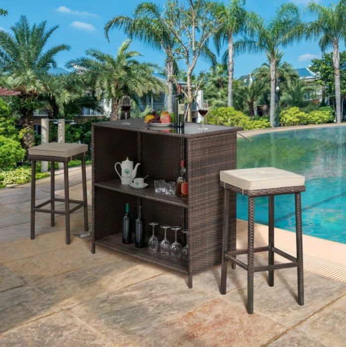A dark rattan bar table with stools, featuring tan cushions, set against a beautifully decorated pool deck — perfect for casual outdoor gatherings.