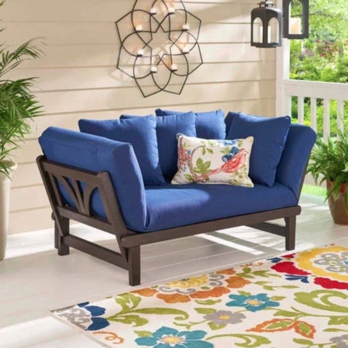 A blue-cushioned daybed arranged as a sofa, placed on a charmingly decorated porch, offering a perfect spot to relax.