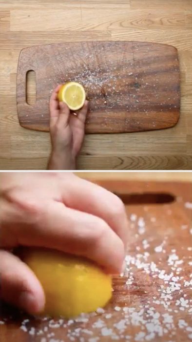 A hand rubs a half lemon over a salt-covered wooden cutting board.