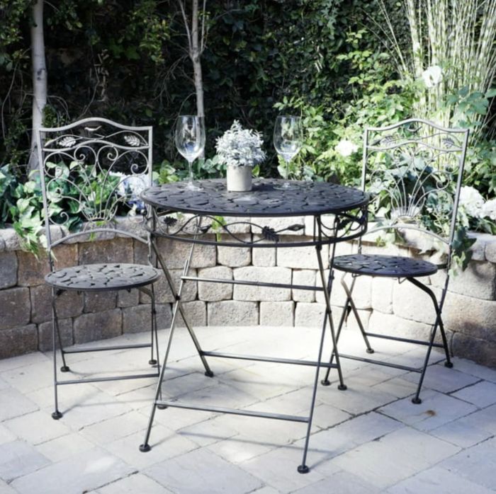 Black metal folding chairs and a matching table, stylishly placed in a decorated patio space.