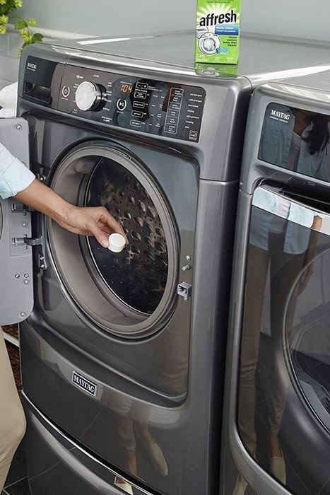 A model dropping a white cleaning tablet into a front-loading washer.