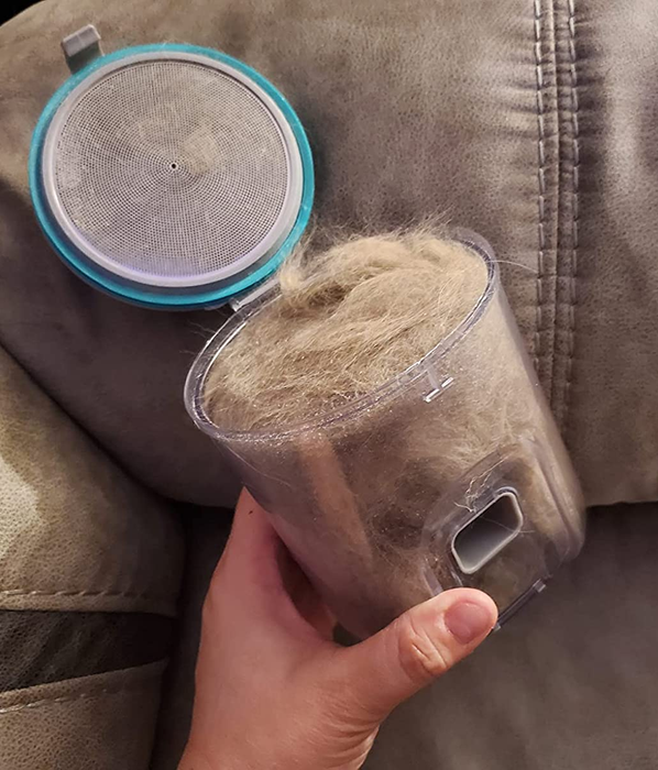 A hand holding the vacuum canister filled with cat hair.