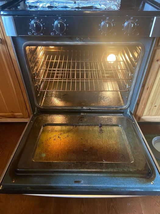 Open oven in a kitchen with wooden cabinets, showing a dirty oven bottom and racks