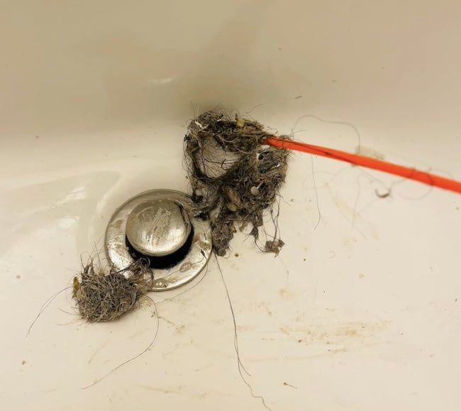 A clogged drain with hair and debris visibly being pulled out.