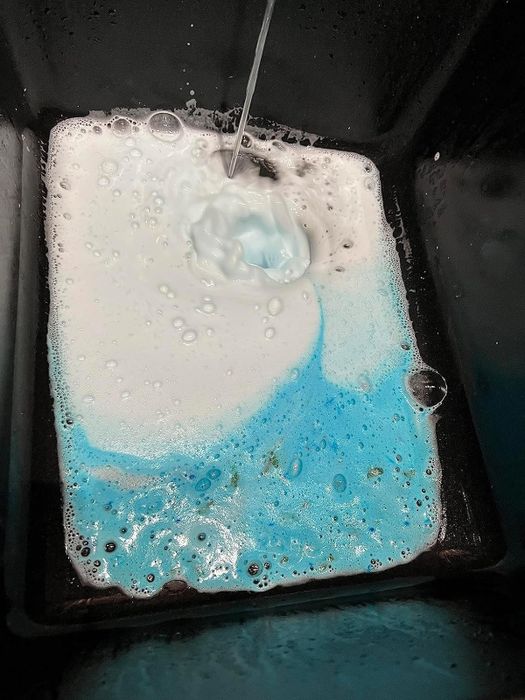 Water flowing into a sink filled with soapy bubbles from a garbage disposal cleaner, creating a swirl of white and blue foam