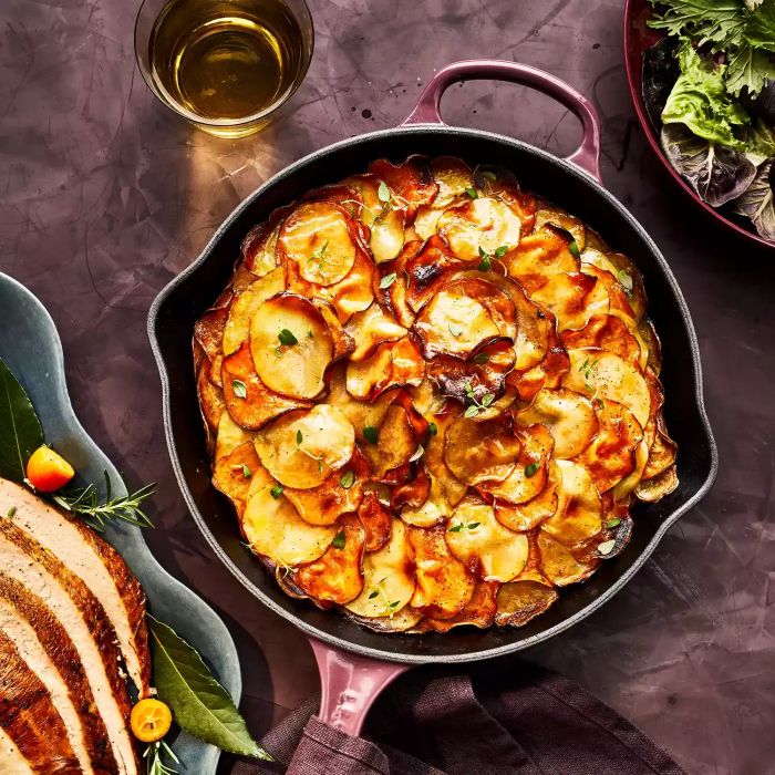 Garlic Herb-Butter Layered Potatoes served in a cast iron dish, set on the table alongside other festive dishes.