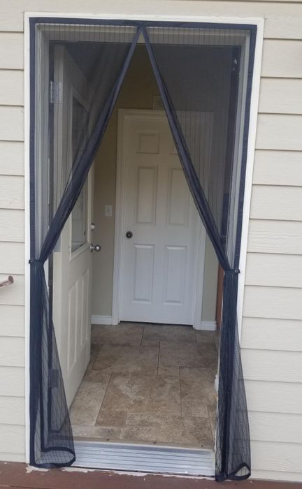 A reviewer's photo showing mesh curtains hanging over an open door frame with hooks keeping them open.