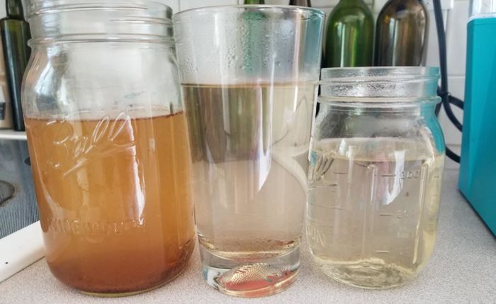 Three glass containers showing the progression of water changing color as it comes out of the machine. From dark brown water on the left to clear, clean water on the right.