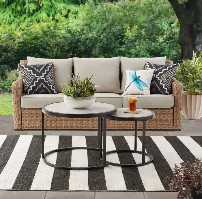 A wicker couch with tan cushions paired with round nesting tables, beautifully arranged in a decorated patio area.