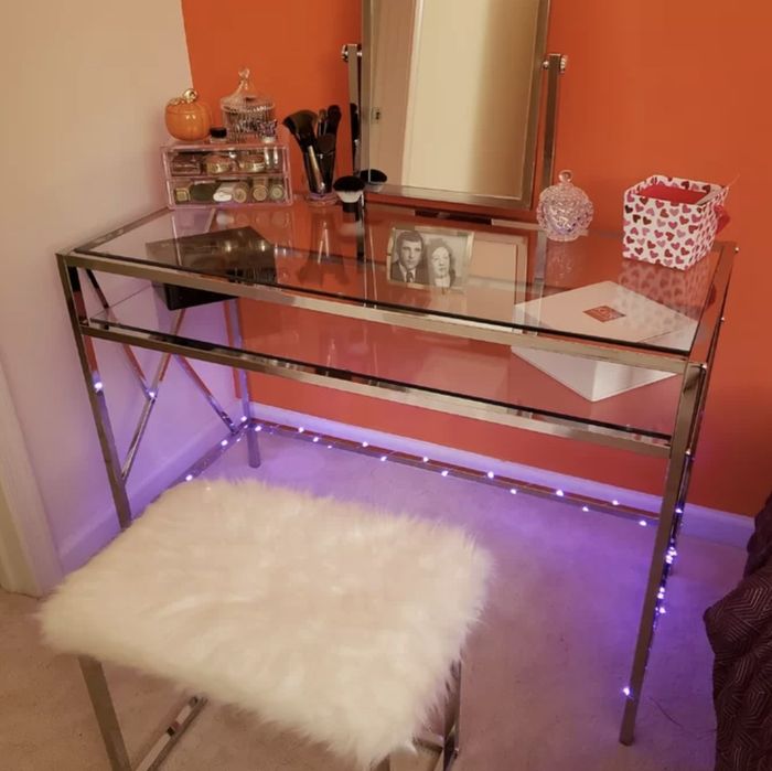 A glass vanity paired with a plush, white fluffy stool.