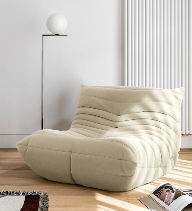 Cream-colored, curved beanbag lounge chair with horizontal pleats placed on a hardwood floor