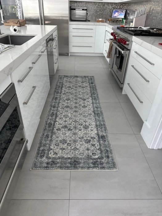 A modern kitchen with white cabinets, sleek appliances, and a patterned runner rug laid out between the countertops.
